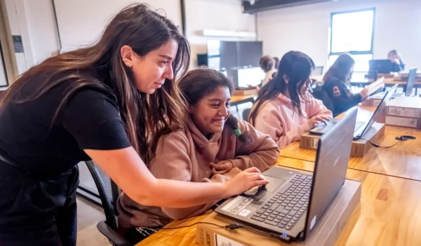Adolescente siendo guiada frente a la computadora por una profesora. Edicion Game Lab del Club de Chicas Programadoras en ATICMA Mar del Plata